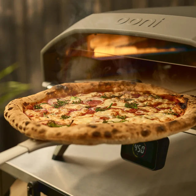 Pizza being cooked in a portable Doni pizza oven with a digital display showing temperature.