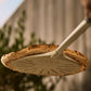 Person holding a pizza oven with a pizza on top against a blurred outdoor background