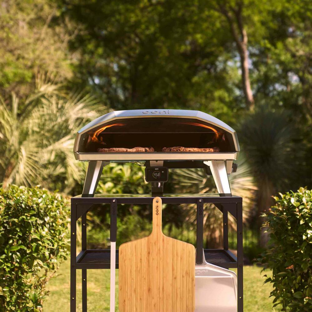 Outdoor pizza oven with a wooden paddle on a stand in a garden setting