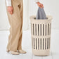 Person holding a gray garment over a beige laundry basket on a white background