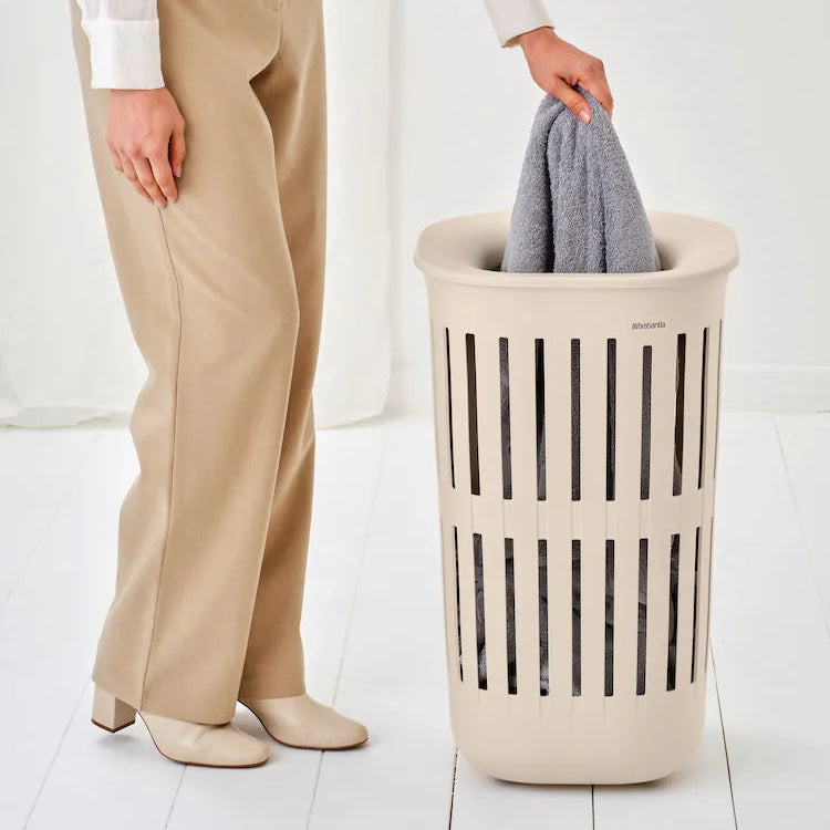 Person holding a gray garment over a beige laundry basket on a white background