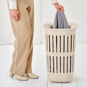 Person holding a gray garment over a beige laundry basket on a white background